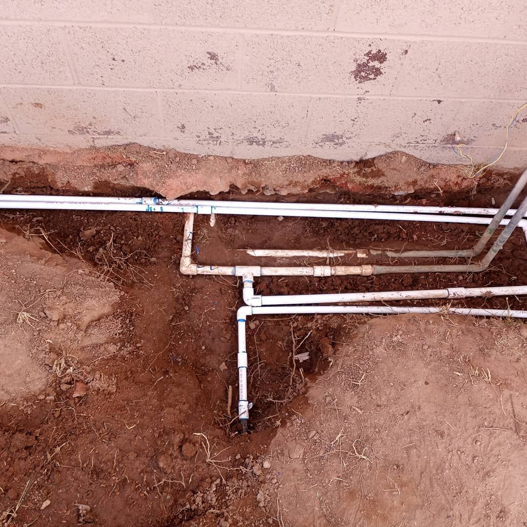 A bunch of pipes are laying in the dirt next to a wall.