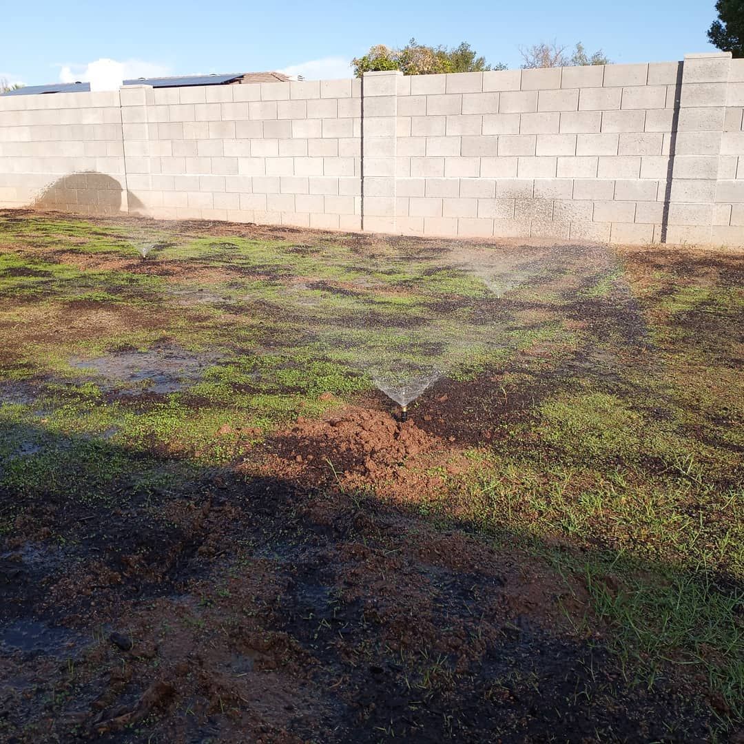 A sprinkler is spraying water on a lush green lawn in front of a brick wall.