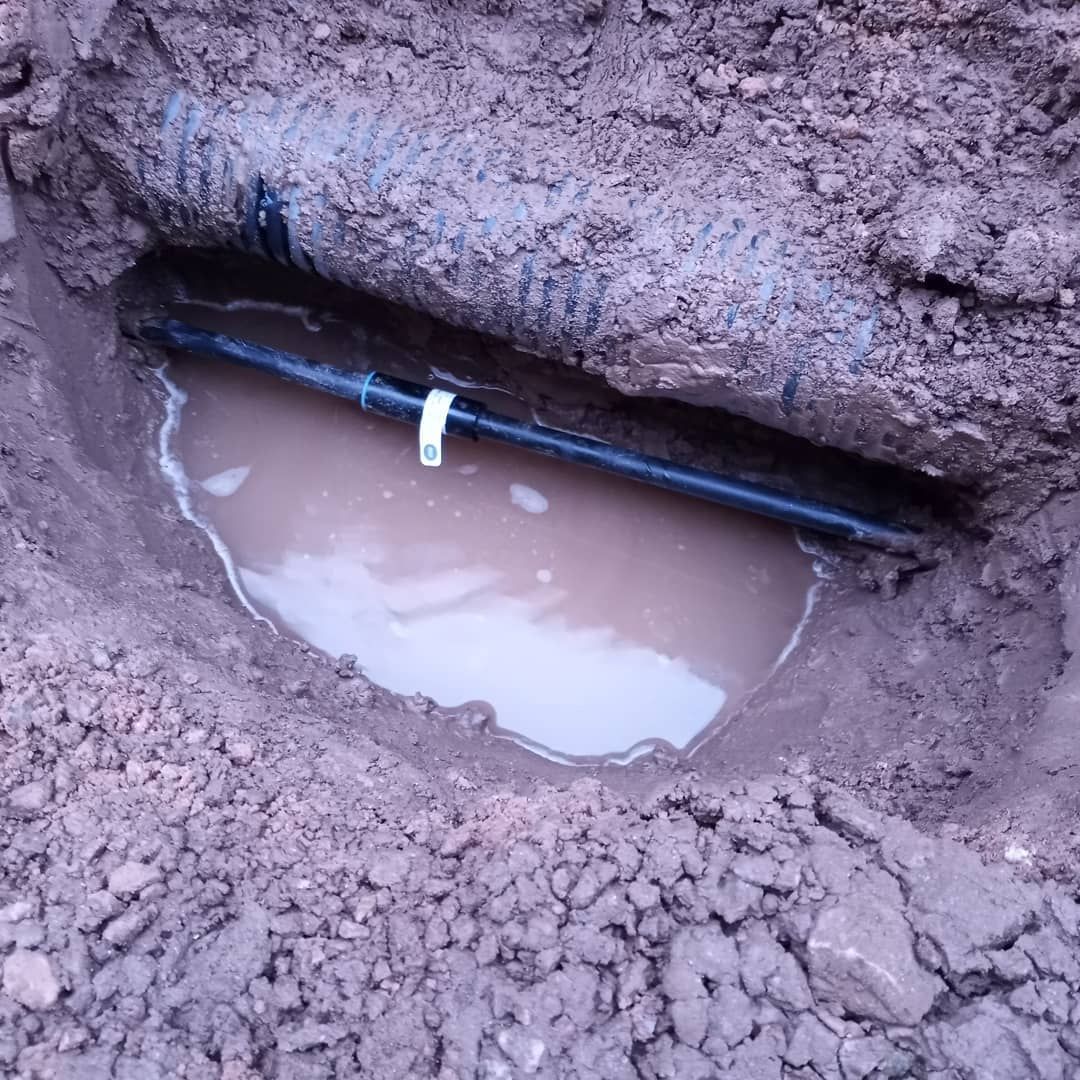 A pipe is laying in the dirt next to a puddle of water.
