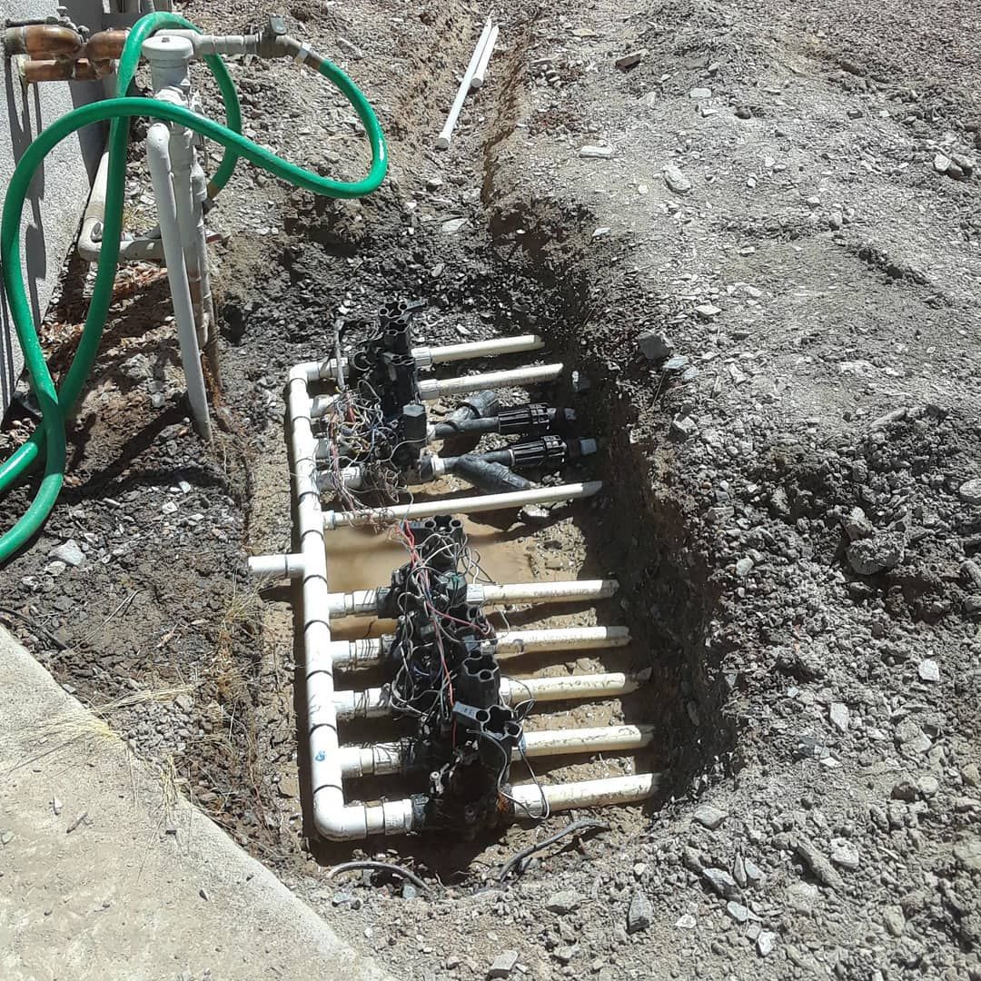 A bunch of pipes are laying in the dirt next to a green hose