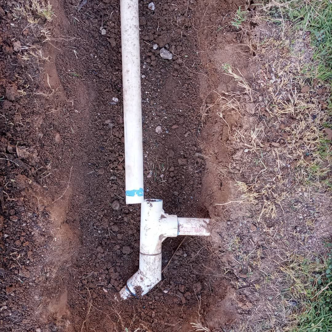 A white pipe is sitting in the dirt next to a grassy area.