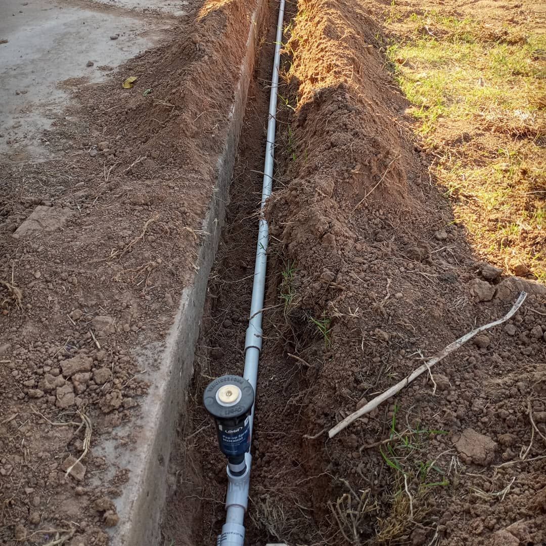 A pipe is laying in the dirt next to a concrete curb.