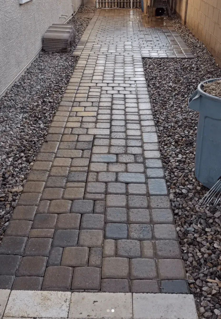 A brick walkway with a trash can on the side of it.