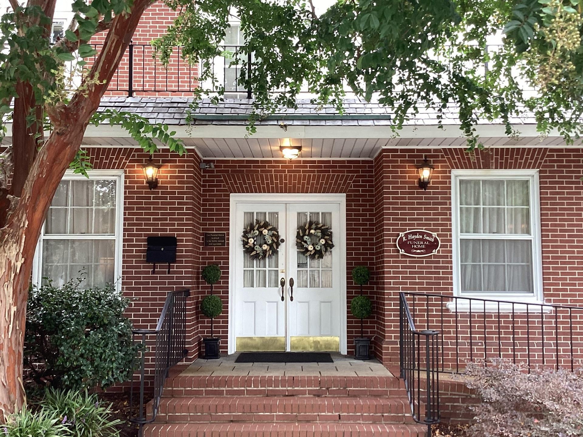 Red brick building entrance with double white doors, wreaths, and steps.
