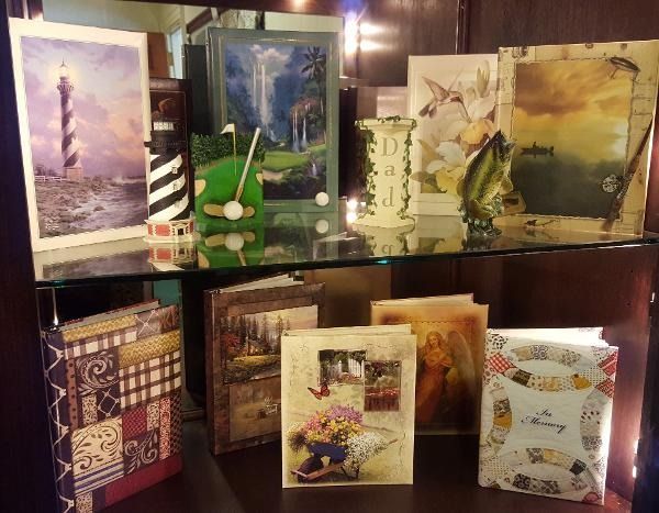 Shelved art prints and decorative objects displayed within a wooden cabinet. Includes a lighthouse, golf figurines, and nature scenes.