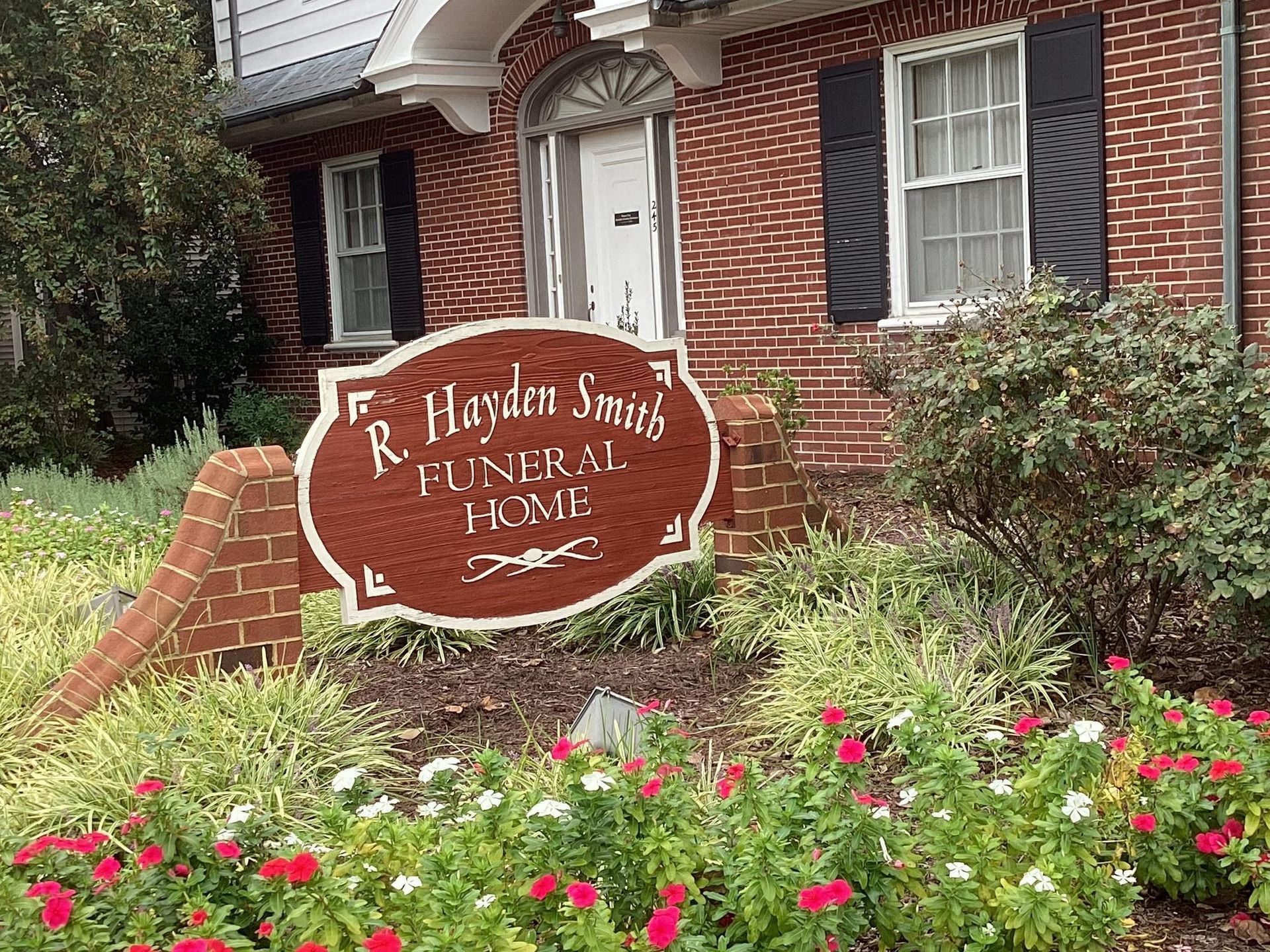 Sign for R. Hayden Smith Funeral Home in front of a red brick building with windows and landscaping.