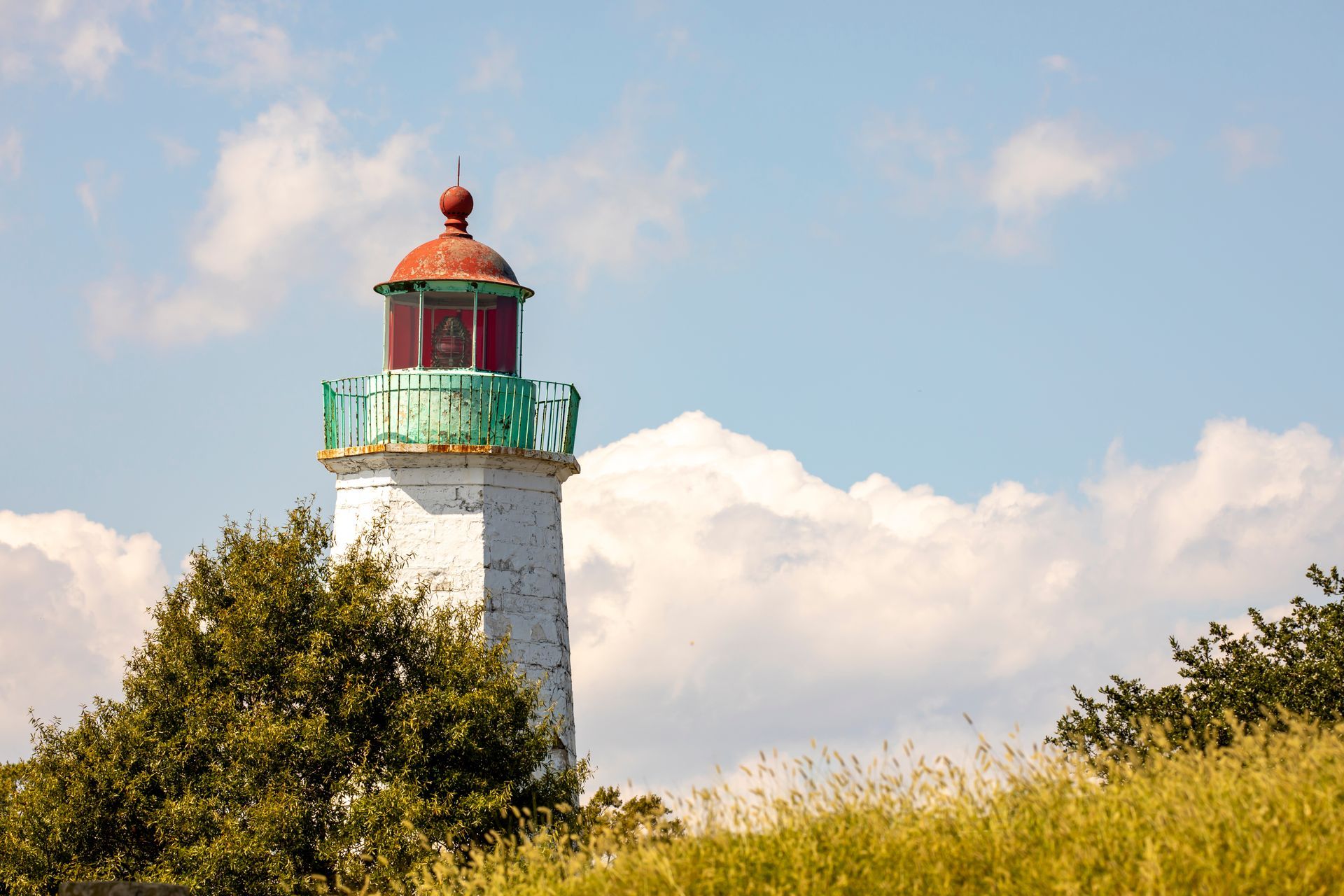White lighthouse with red top and green accents against a blue sky with clouds.