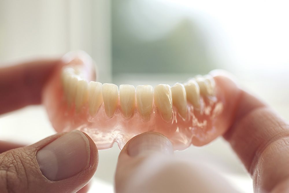Dental technician using a tool to work on a set of dentures with attached implants.