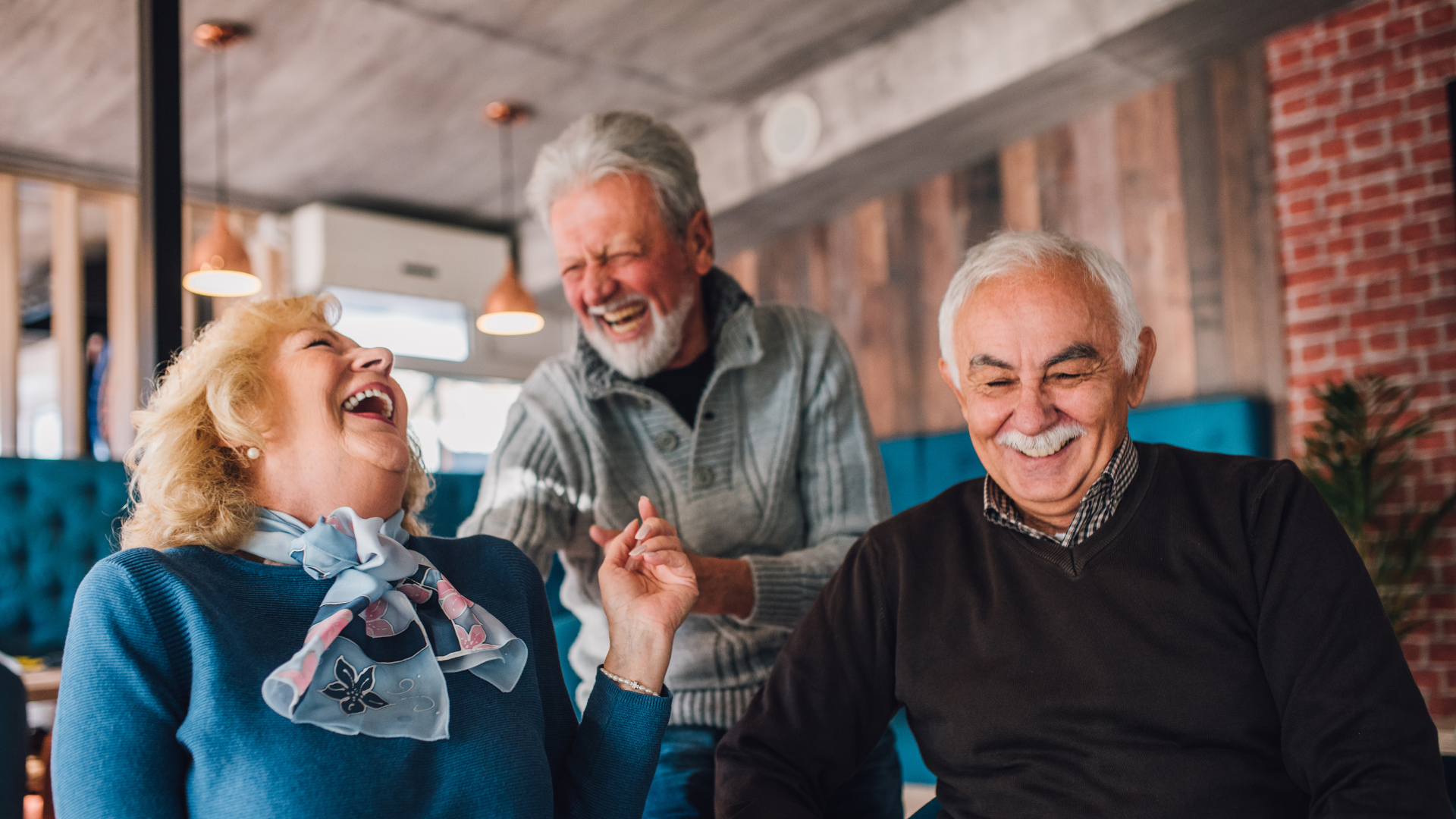 Three older adults laughing together indoors, a cafe setting.