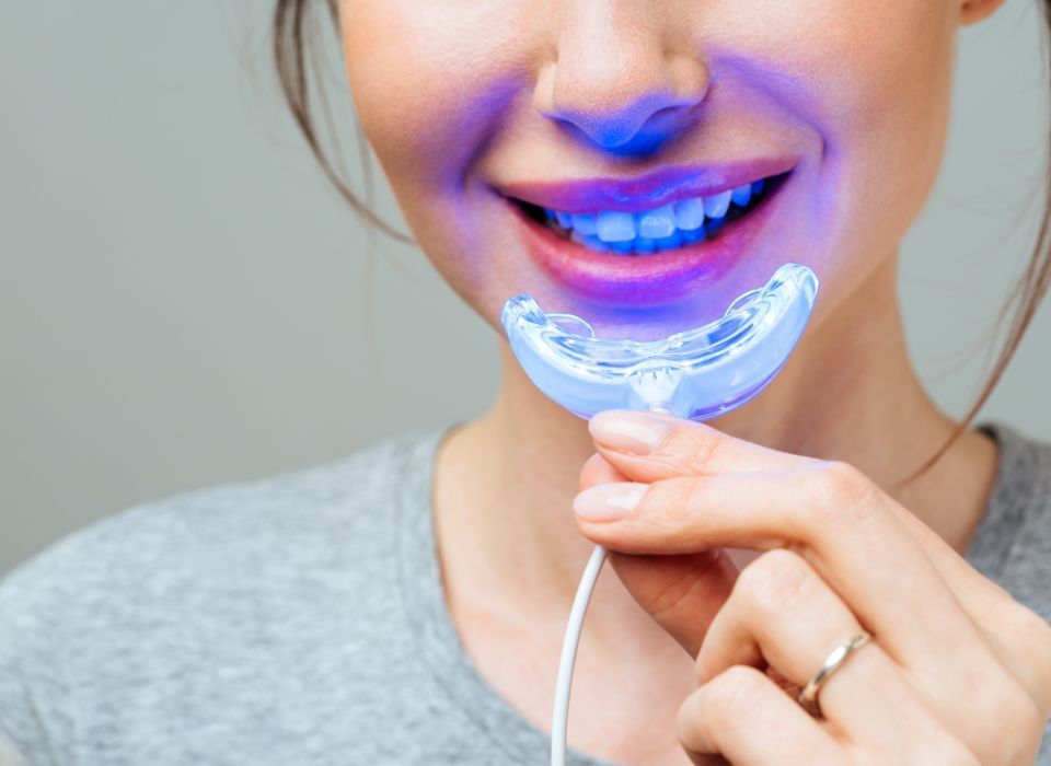 Hand holding a model showing dentures attached to dental implants, with pink gums and white teeth.