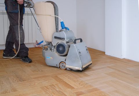 Worker sanding a hardwood parquet floor with a floor grinder