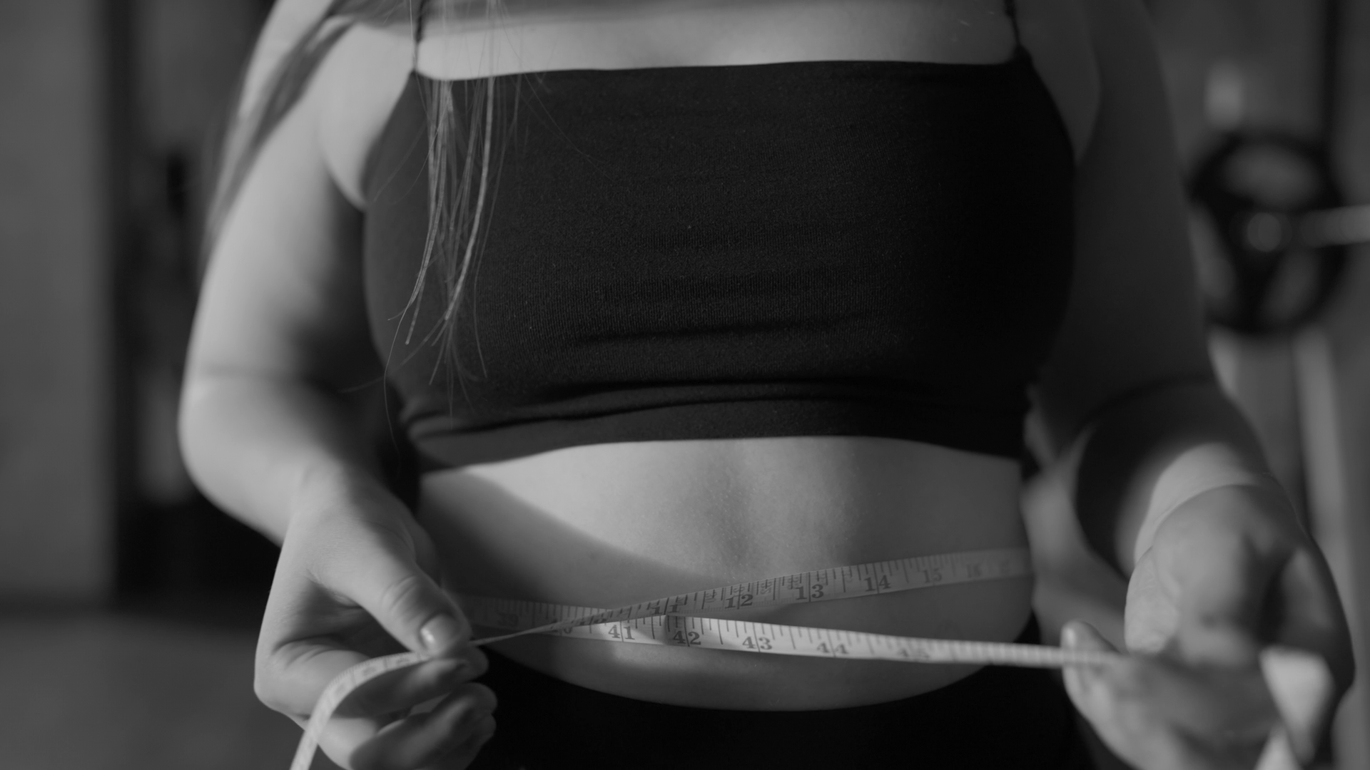 Woman in a black sports bra measuring her waist with a tape measure.
