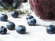 A close up of blueberries and a smoothie in a glass on a table.