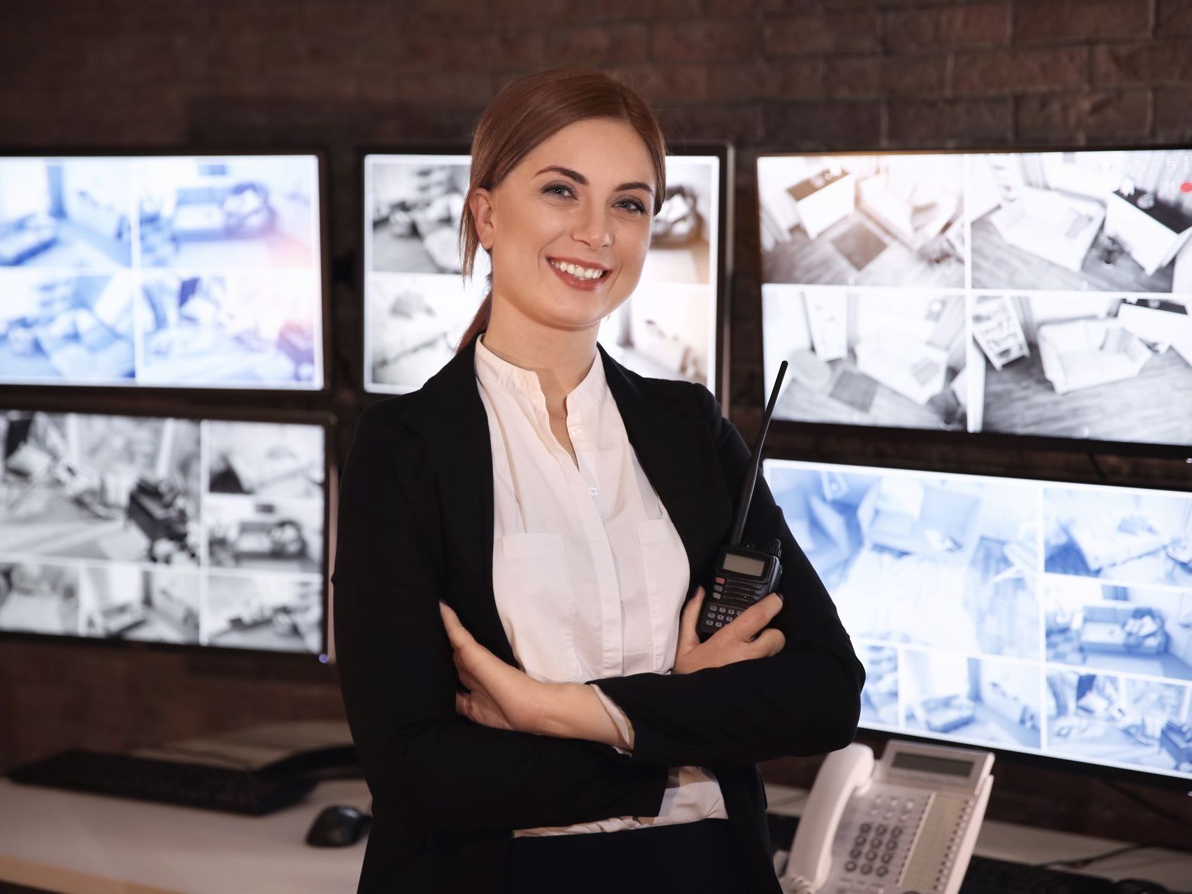A woman is standing in front of a bunch of monitors with her arms crossed.
