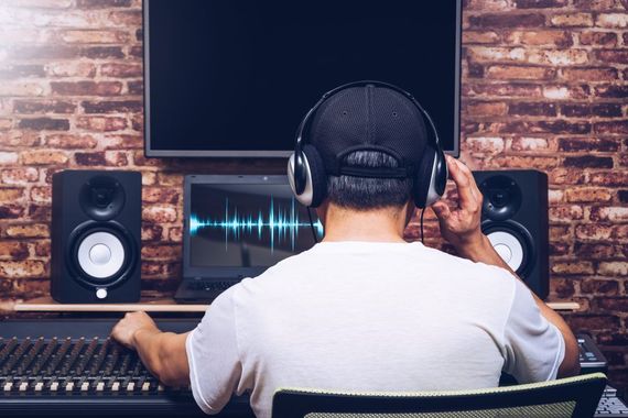 A man wearing headphones is sitting in front of a computer in a recording studio.