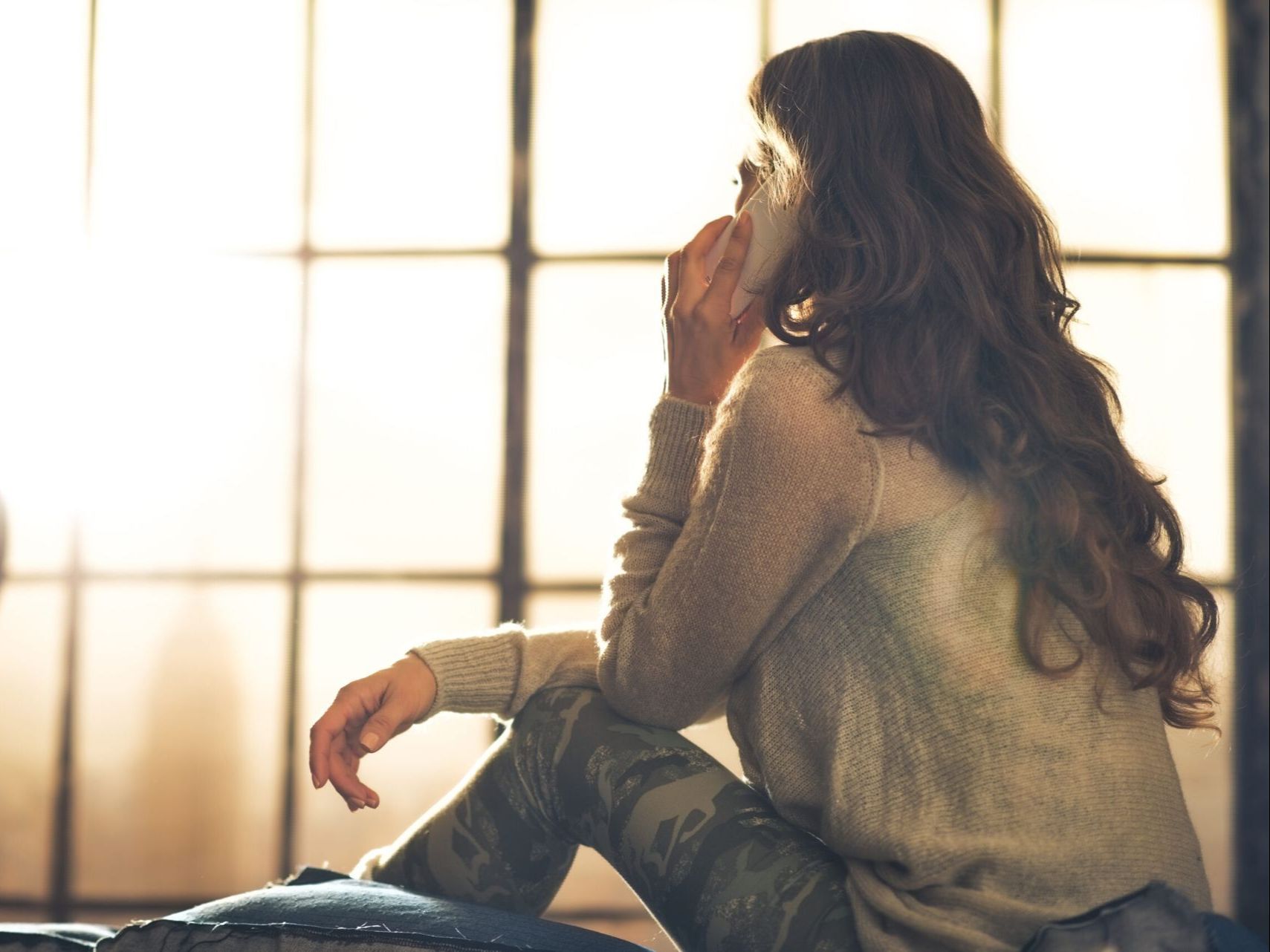 A woman is sitting on a couch talking on a cell phone.