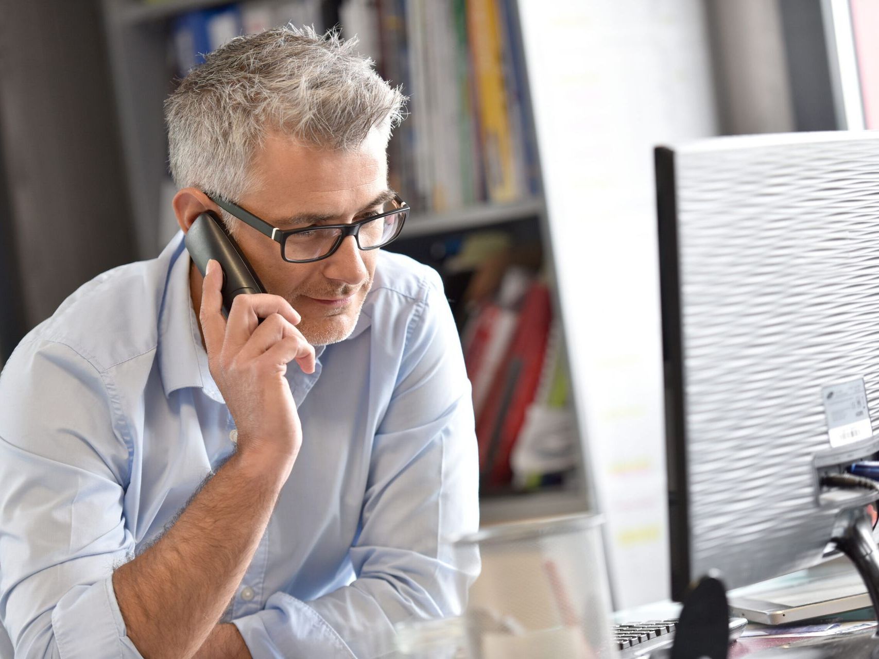 A man is sitting at a desk talking on a cell phone.