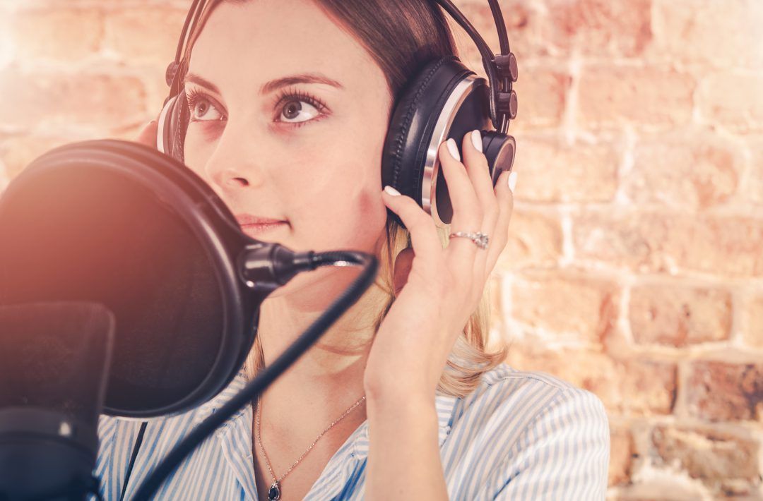 A woman wearing headphones is singing into a microphone.