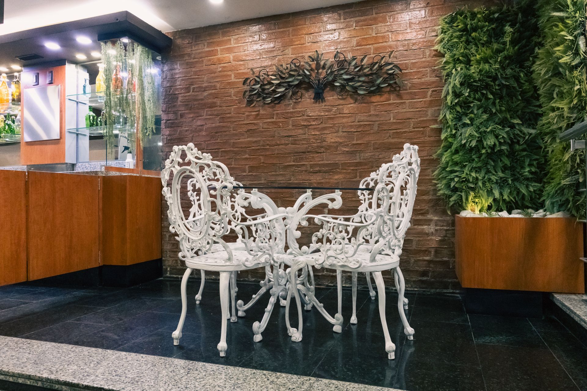 Two white chairs and a table are sitting in front of a brick wall.