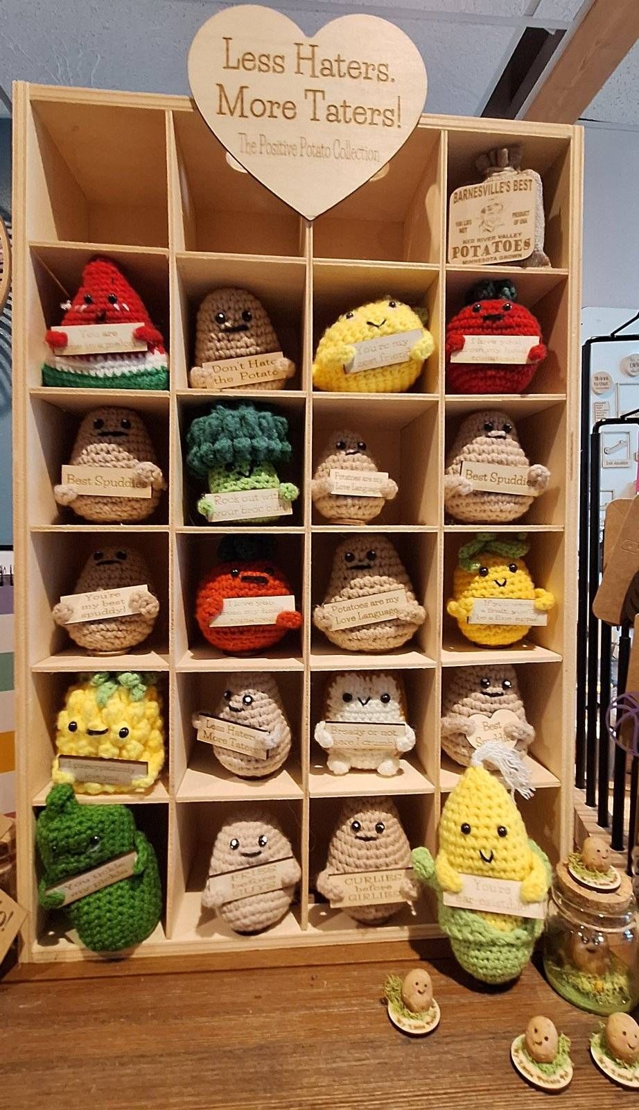 A wooden shelf displaying crocheted vegetable figures with happy faces, each in its own cubby.