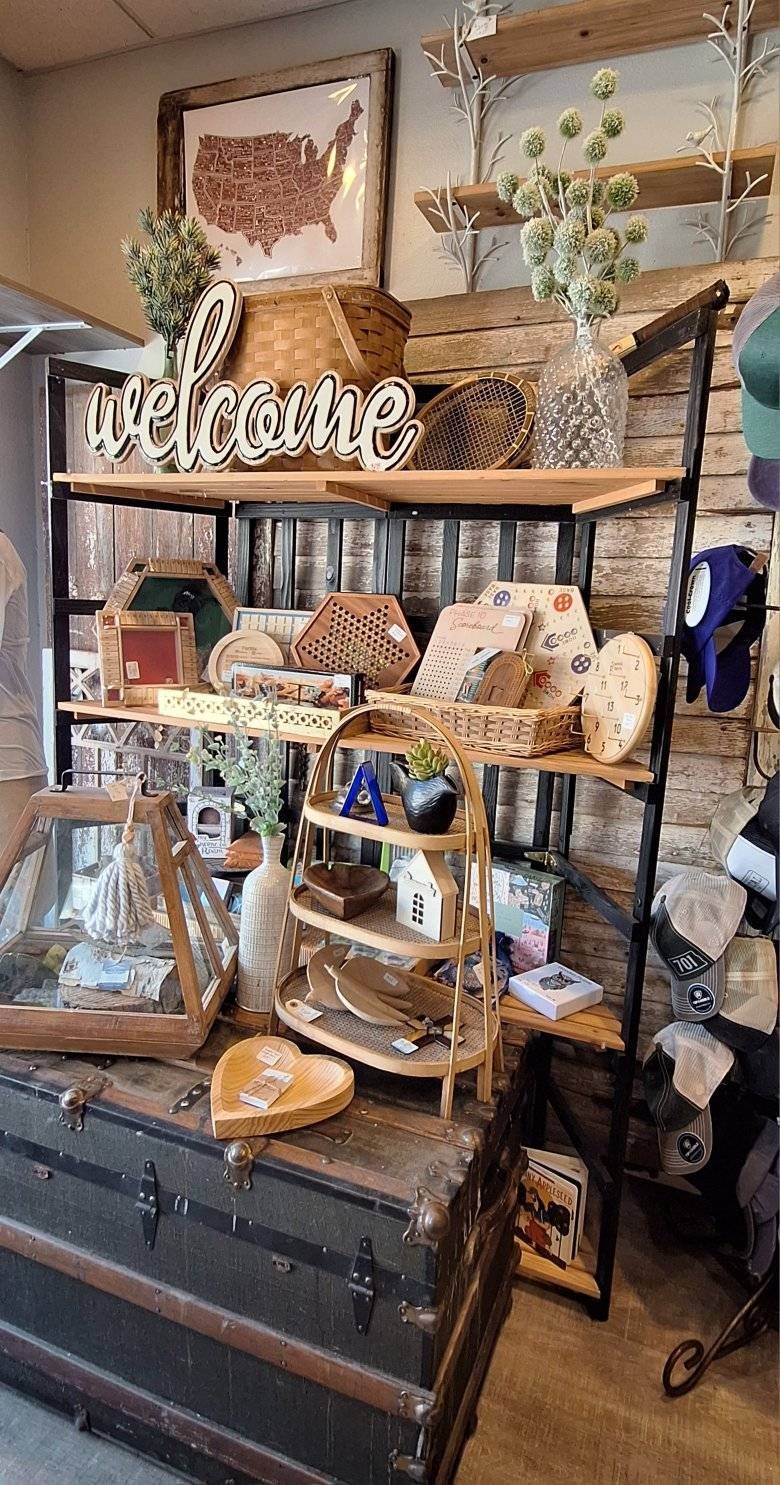 Shop display with shelves of goods and a welcome sign; antique trunk in front.