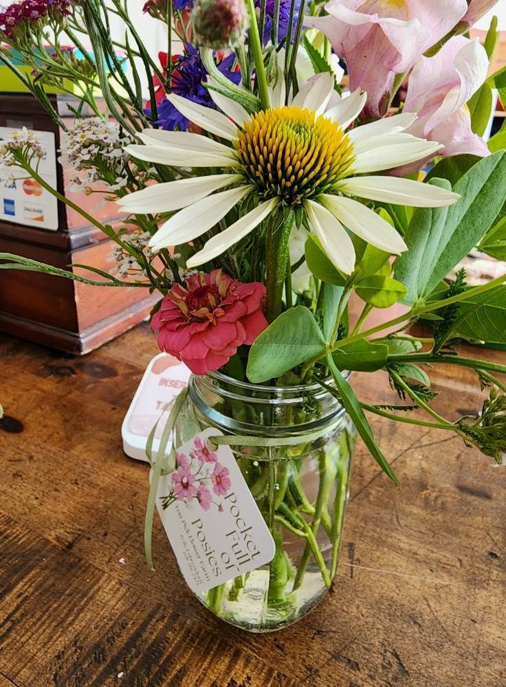 Flower arrangement in a clear jar on a wooden table, featuring a white coneflower and other colorful blooms.
