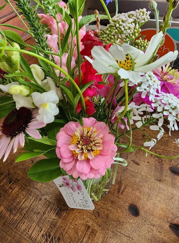 Colorful floral bouquet in a vase on a wooden table, featuring pink and white blooms.