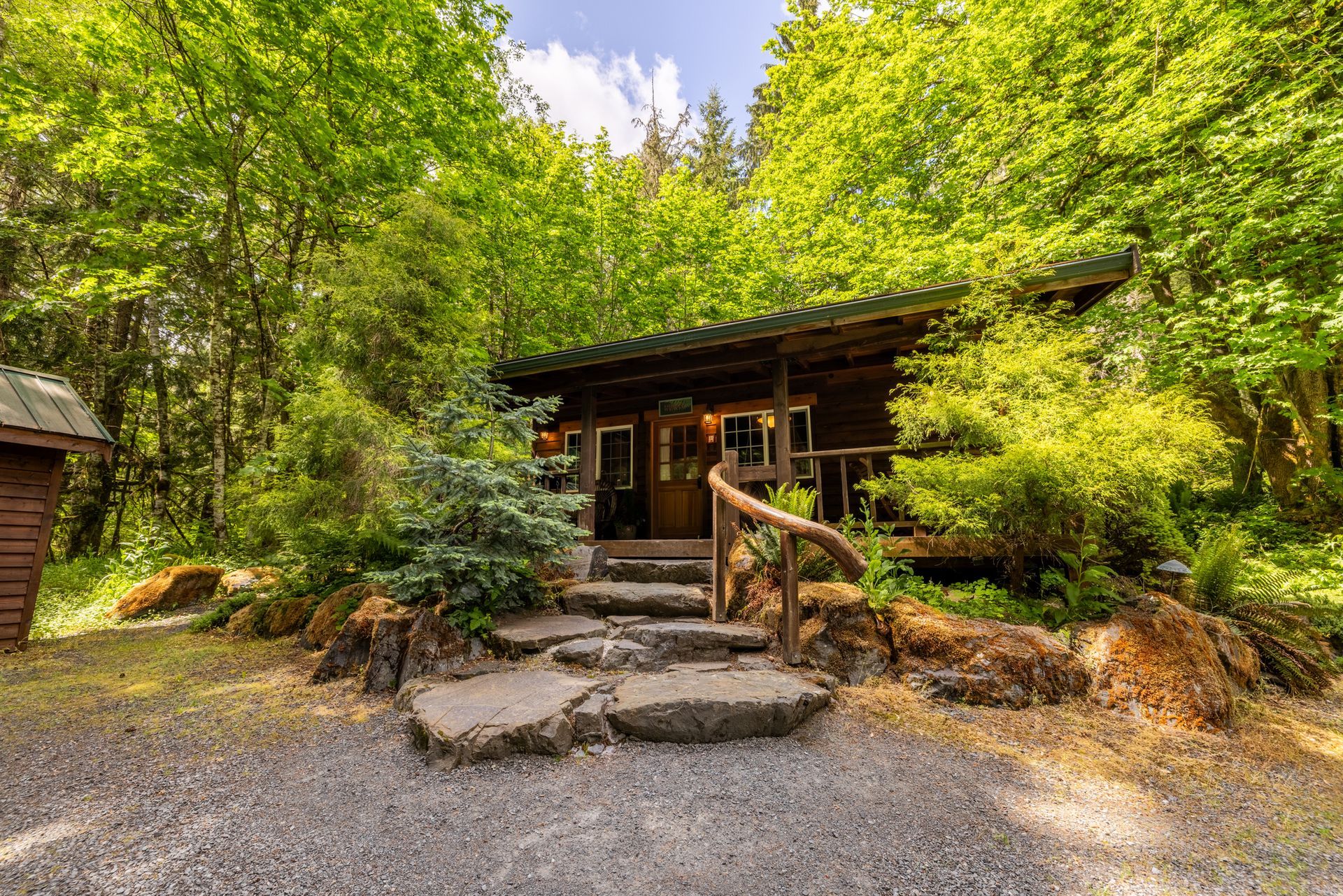 A small wooden cabin in the middle of a forest with stairs leading up to it.