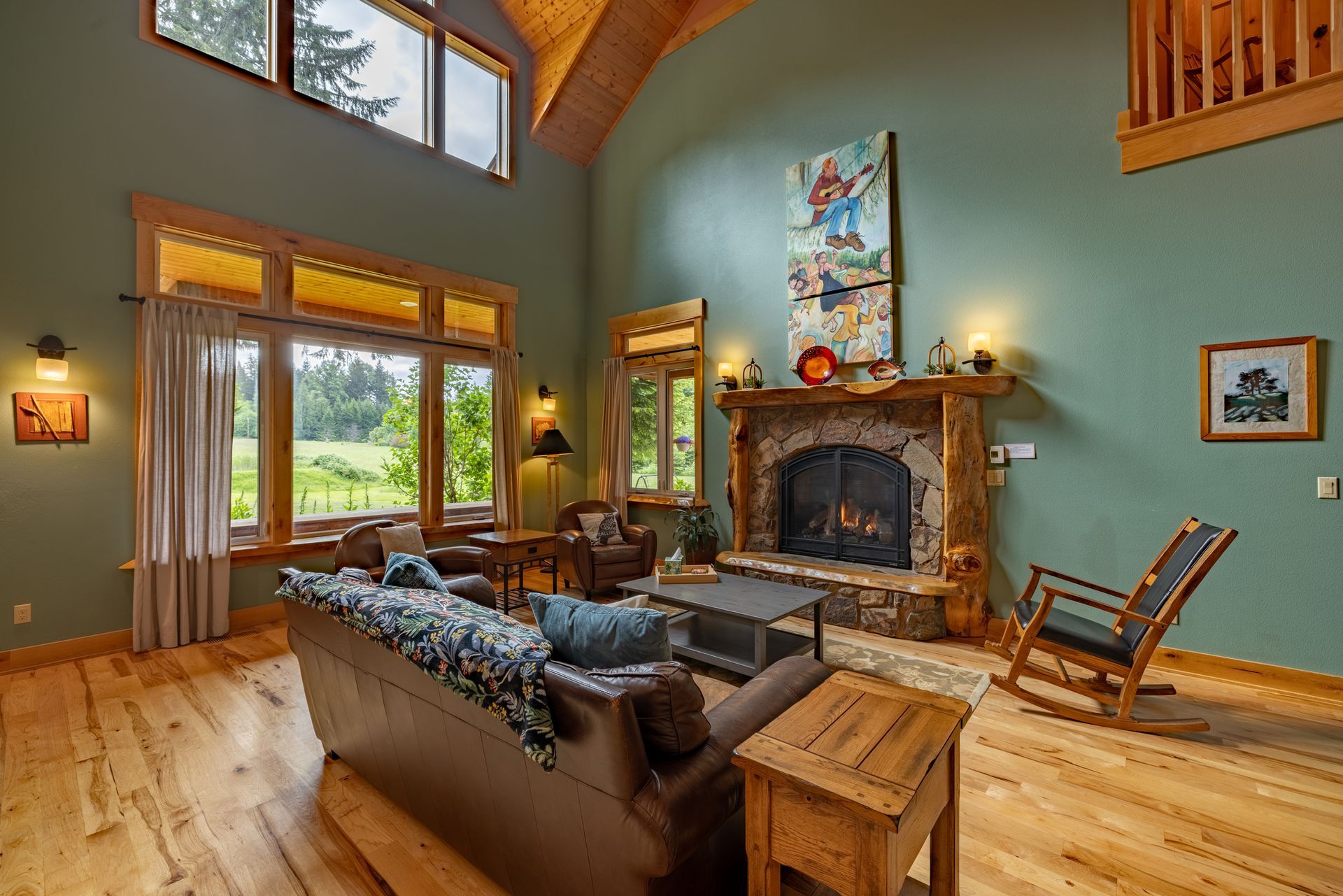 A spacious living room with a fireplace, leather sofa, and large windows overlooking a green field.