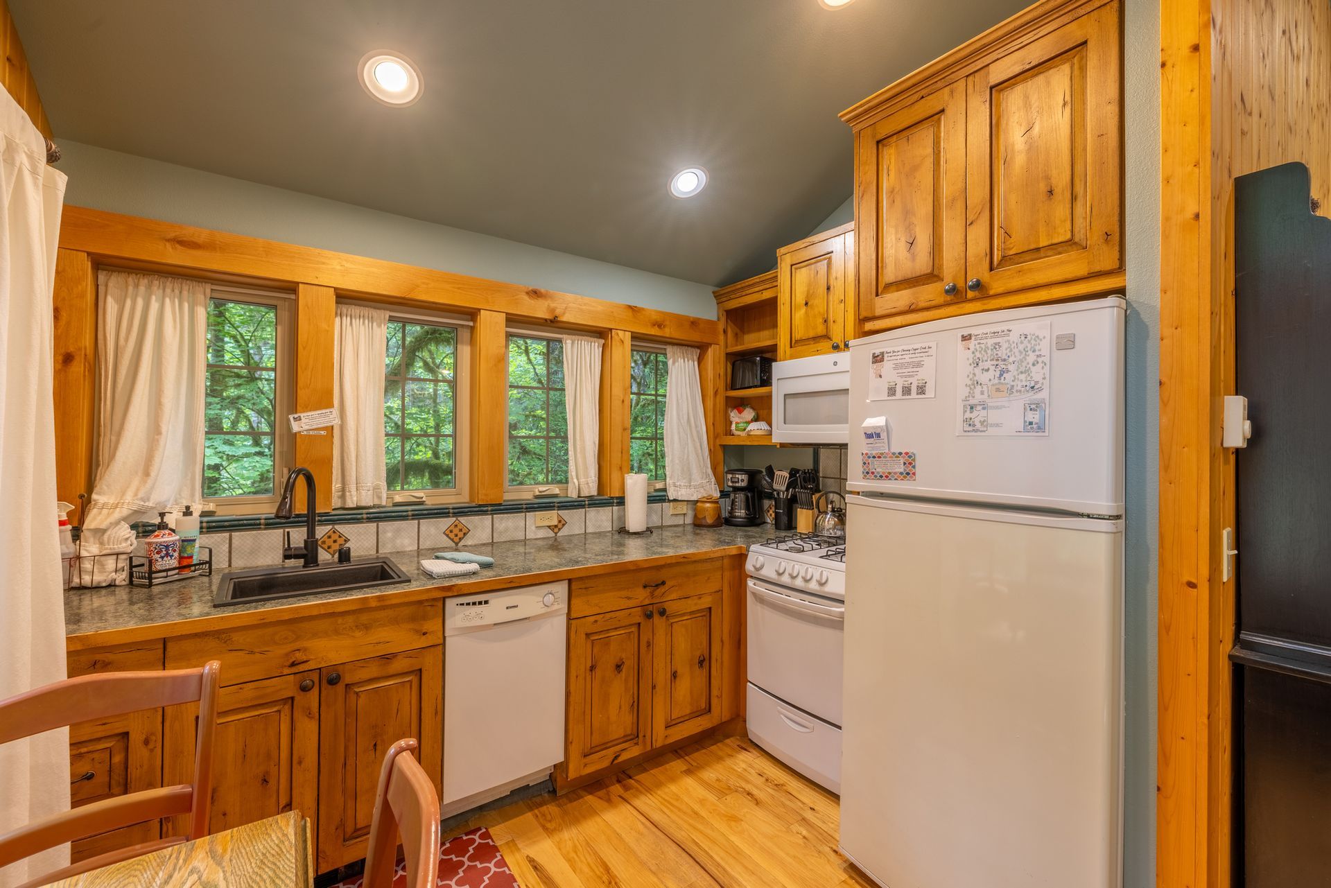 Cozy kitchen with wooden cabinets, appliances, and windows overlooking greenery.