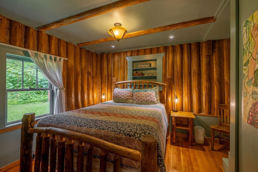 A rustic bedroom with wood-paneled walls, a log bed, and a small window overlooking greenery.