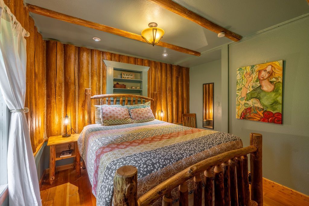 Bedroom with wooden paneling, log bed frame, colorful quilt, and floral painting.