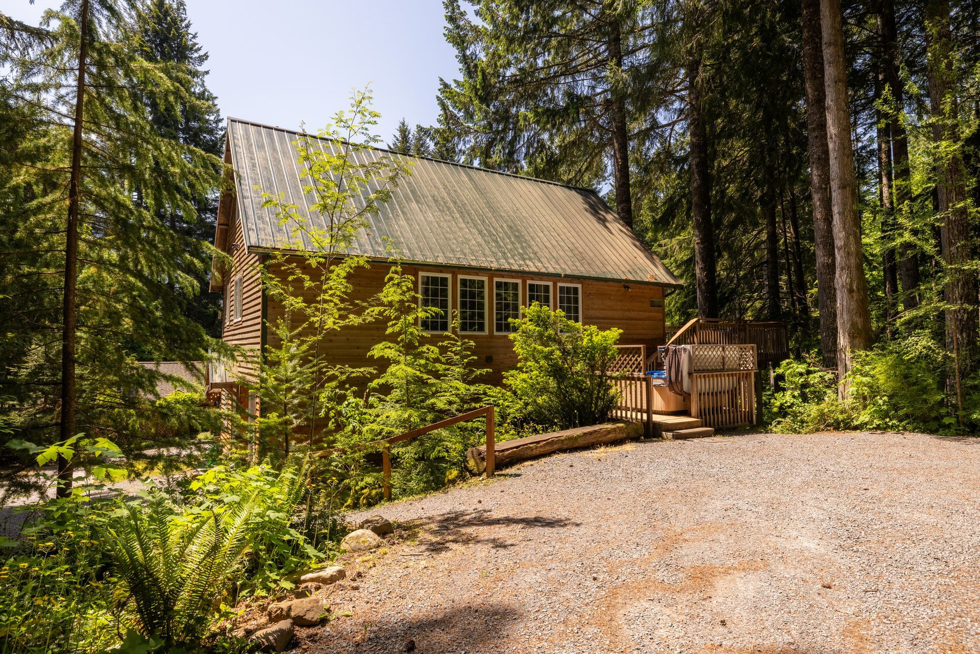 Wooden cabin in a forest setting, with a gravel driveway. Sunny day with lush green trees surrounding the building.
