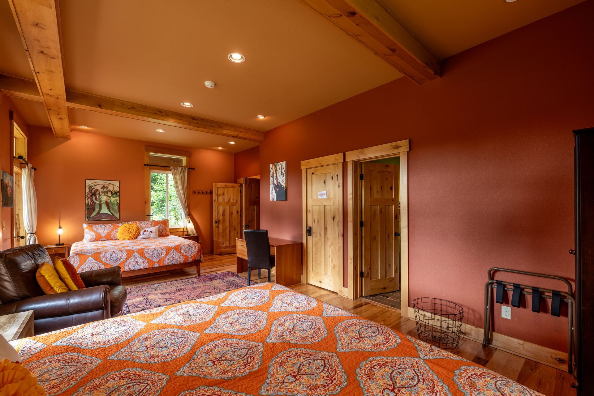 A large hotel room with orange walls, a bed with an orange patterned comforter, a seating area, and wooden accents.