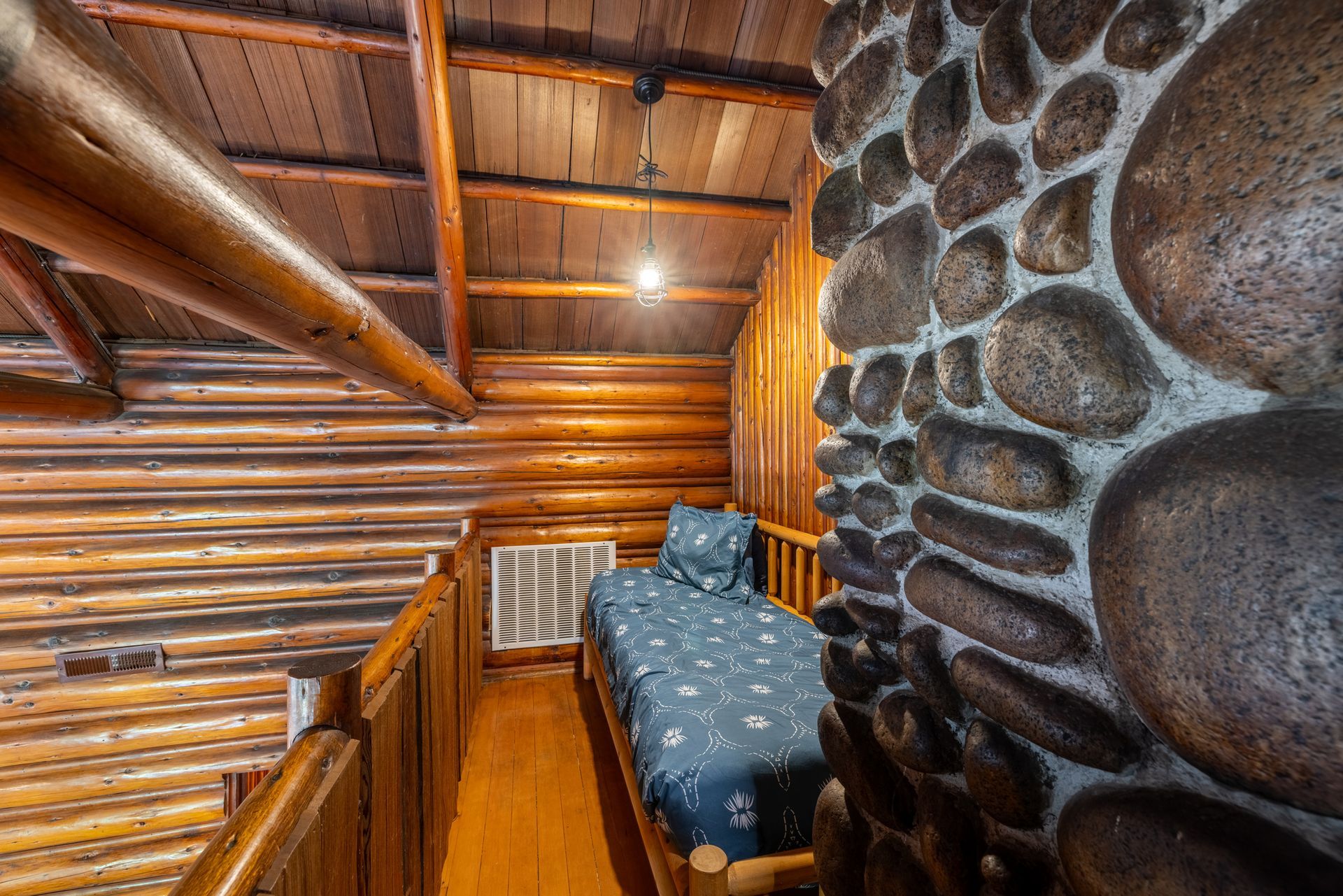 A small, rustic bedroom nook with a single bed. A stone wall and wooden beams dominate the space.