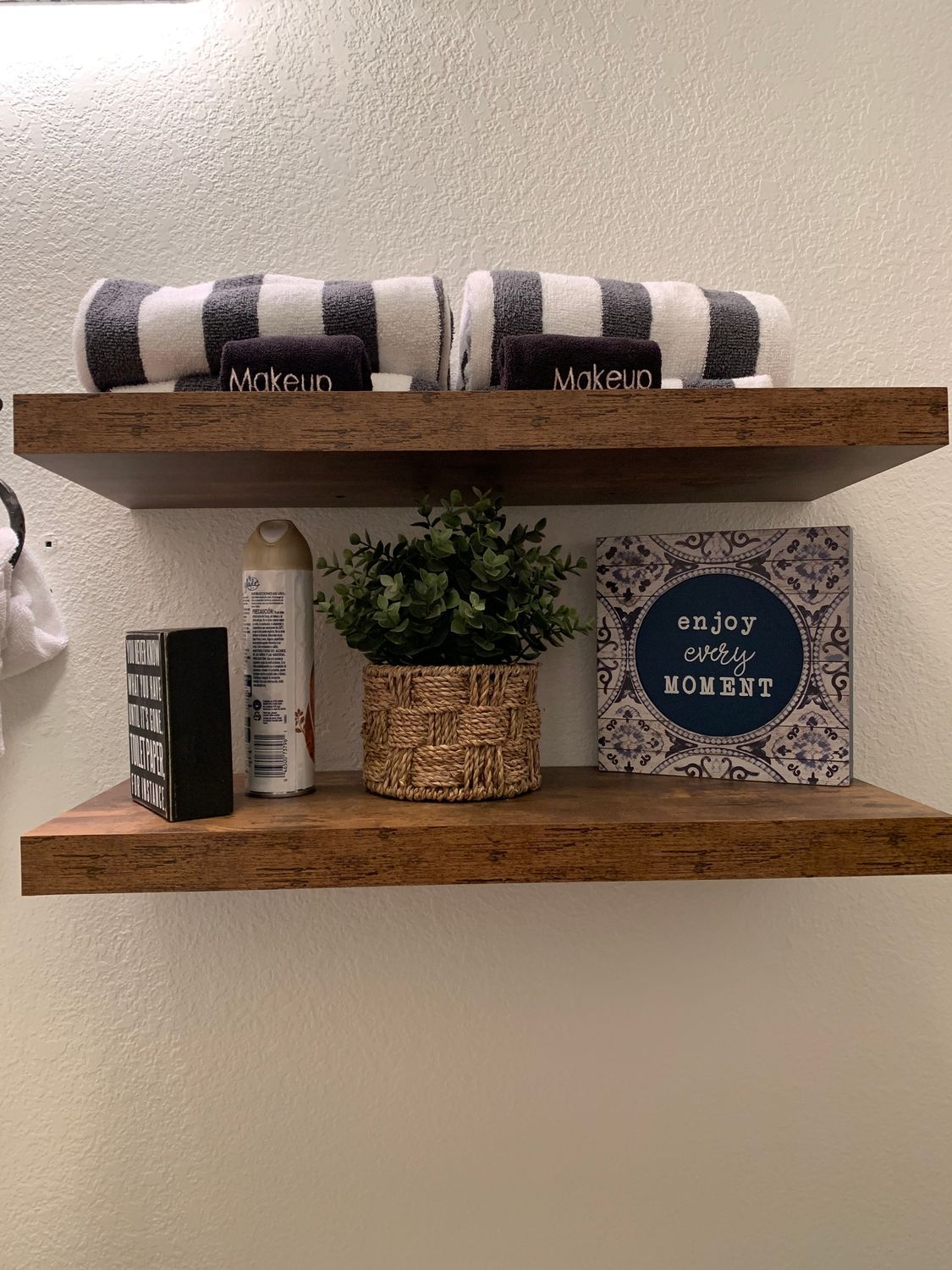 Two wooden floating shelves displaying bathroom decor: towels, a plant, and decorative items.