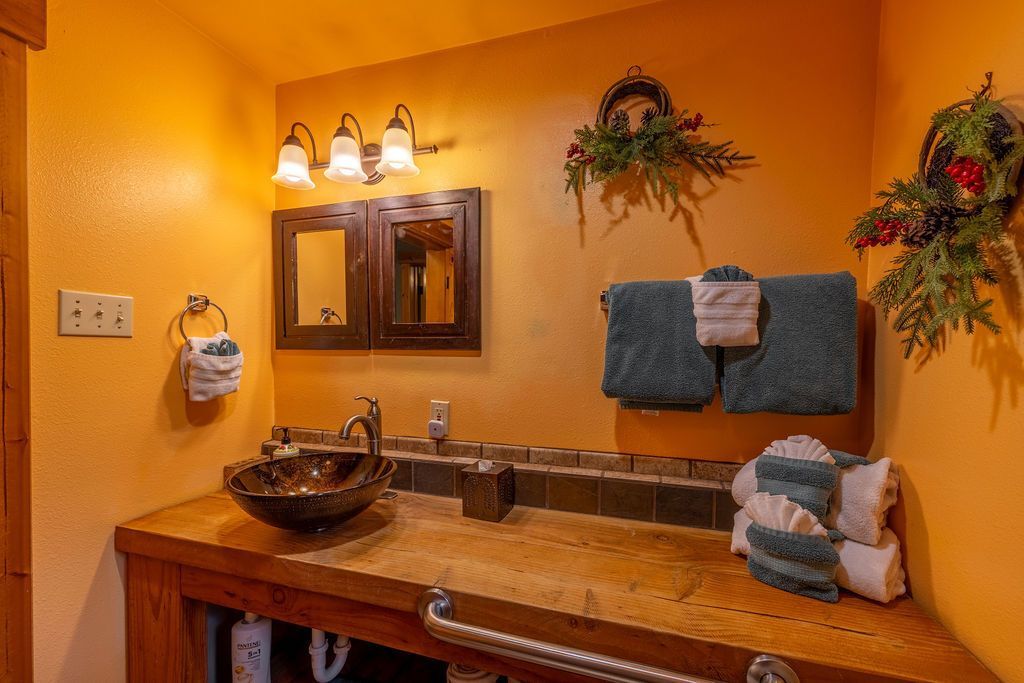 Bathroom with a rustic aesthetic. Features an orange wall, wooden vanity with a patterned sink, and decorative accents.