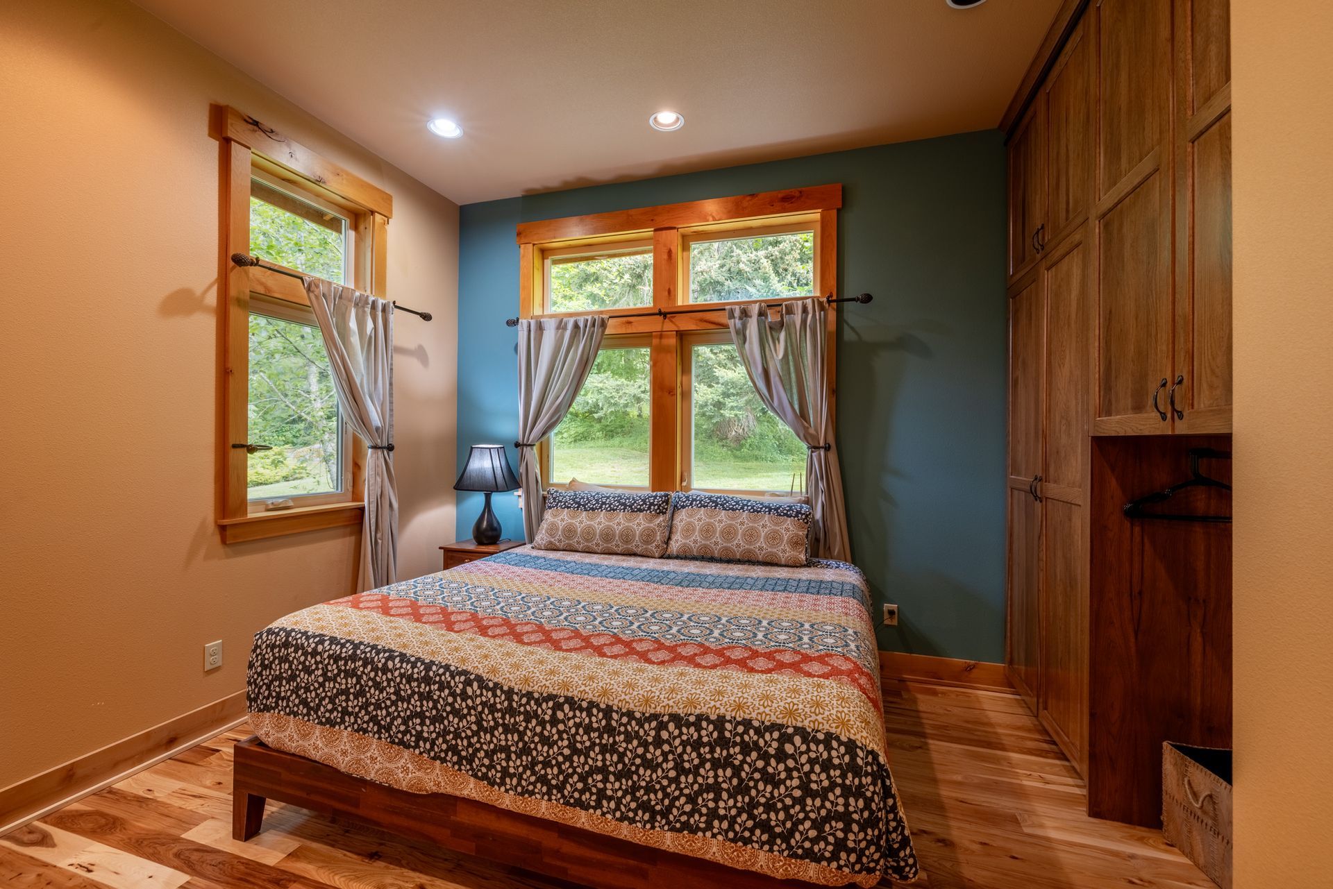 Bedroom with a bed, windows, curtains, and wood furniture. Walls are painted in blue and beige with wood trim.