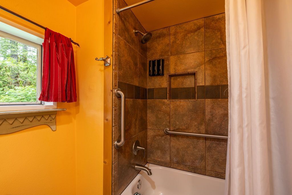Bathroom with orange walls, a window with red curtains, and a tiled shower with grab bars.