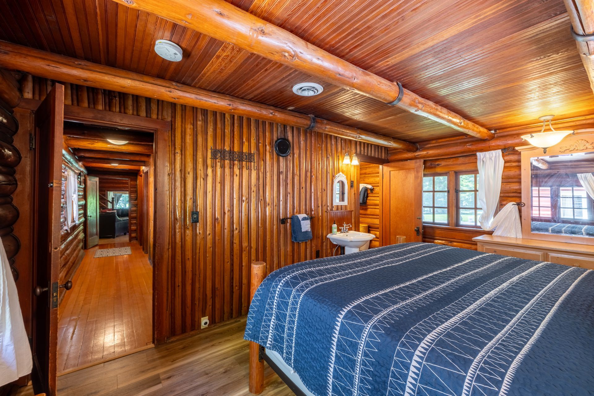 Bedroom with wooden walls and ceiling, a bed with a blue comforter, a sink, and a doorway to a hallway.