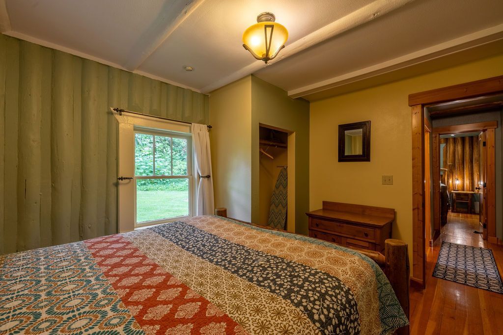Bedroom with a patchwork quilt, green walls, a window, and an entryway to a hallway.