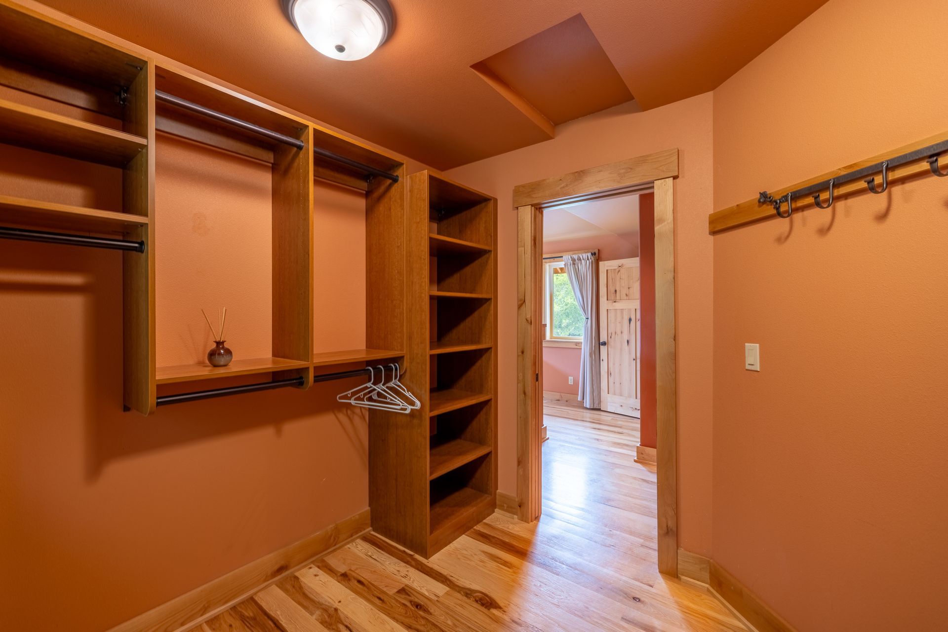 Walk-in closet with shelving, hanging rods, and a doorway leading to a bedroom. The walls and ceiling are orange with wood floors.