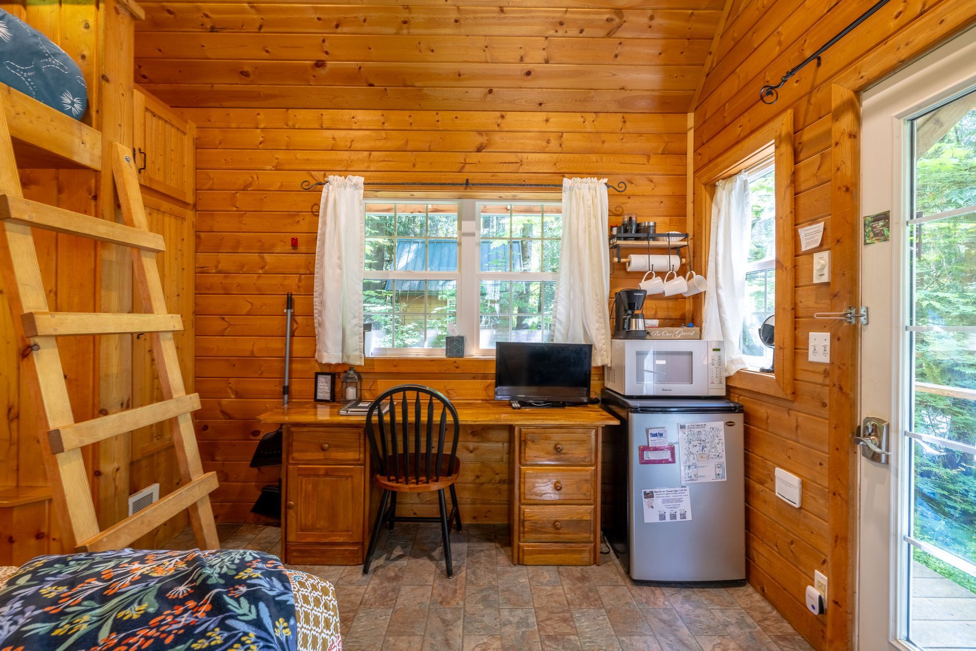 Cozy cabin bedroom with a double bed, bunk bed above, desk, and wooden walls.