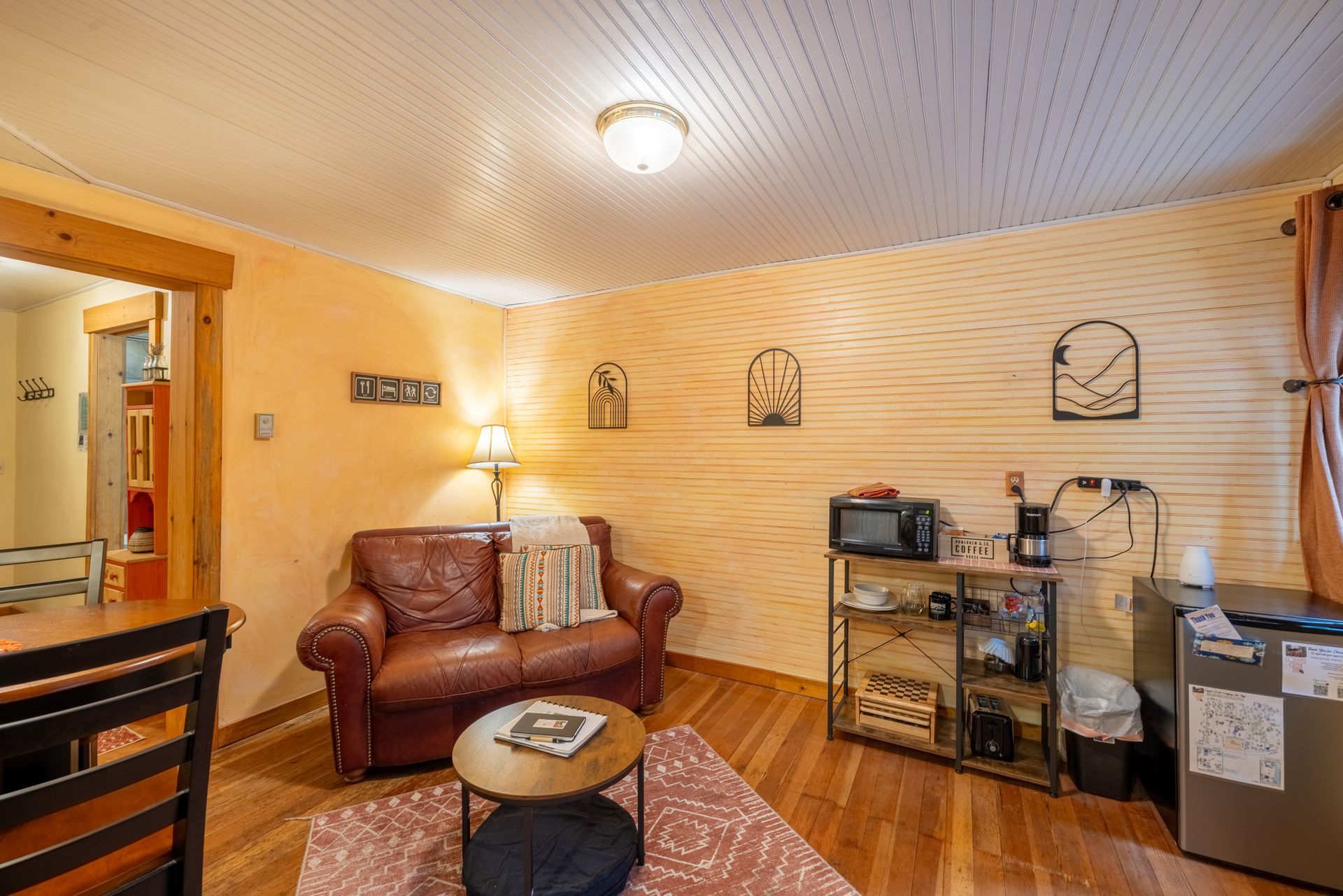 Small cozy living area with leather sofa, wood-paneled wall, and a mini-kitchen area. Warm lighting and decor.