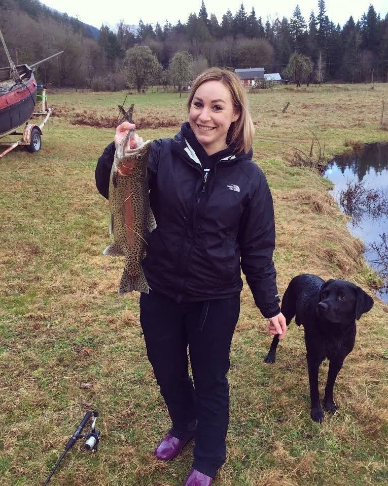 A woman holding a large fish next to a black dog