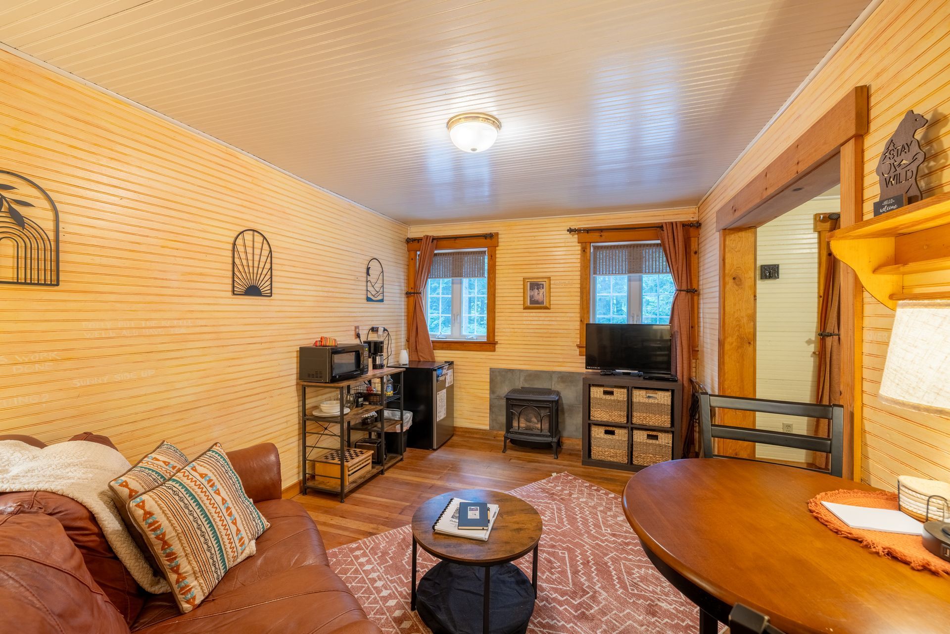 Cozy living room with a brown leather couch, wooden walls, a small dining table, and a TV.