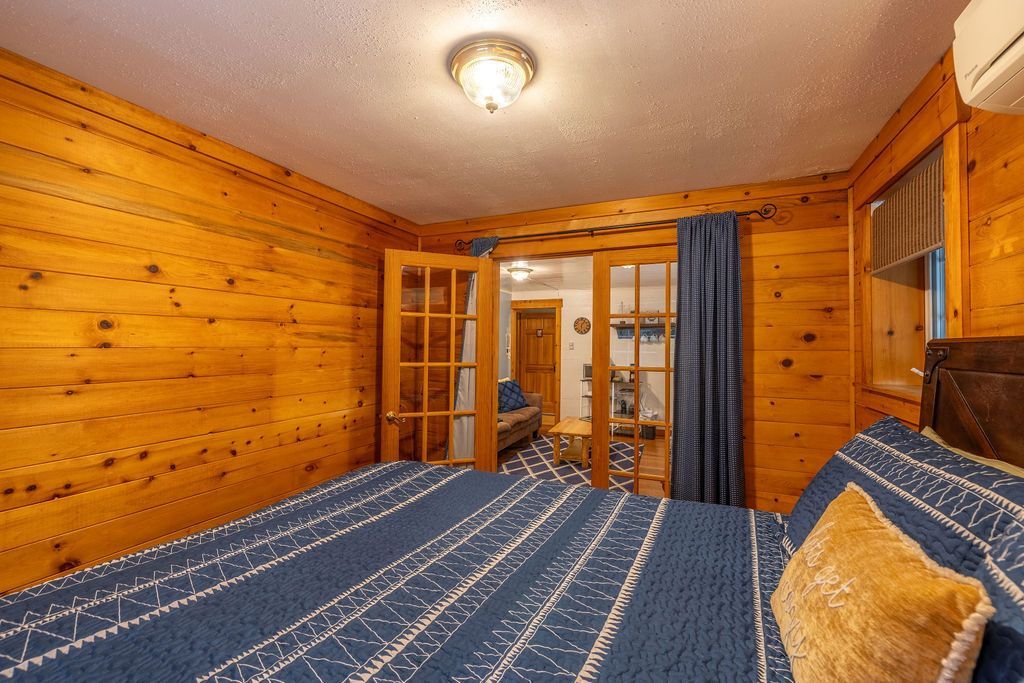 Bedroom with wood-paneled walls, a bed with blue bedding, and French doors leading to another room.