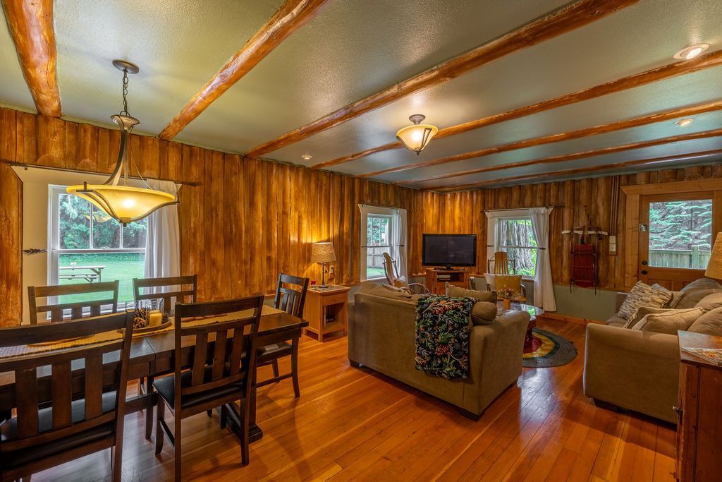 Interior of a rustic living room and dining area with wood walls, ceiling beams, a dining table, sofa, and TV.