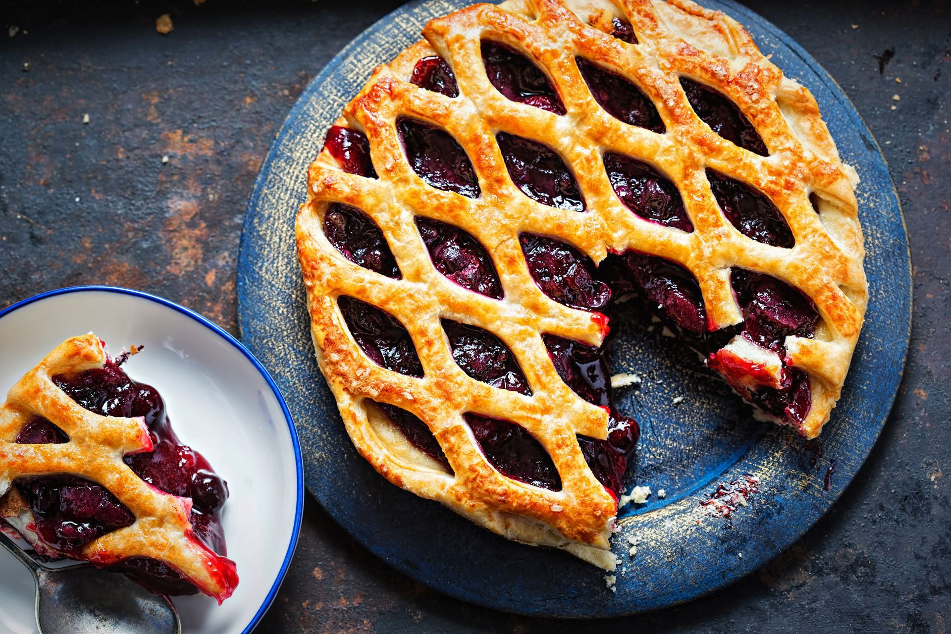 A cherry pie with a slice taken out of it is on a blue plate.