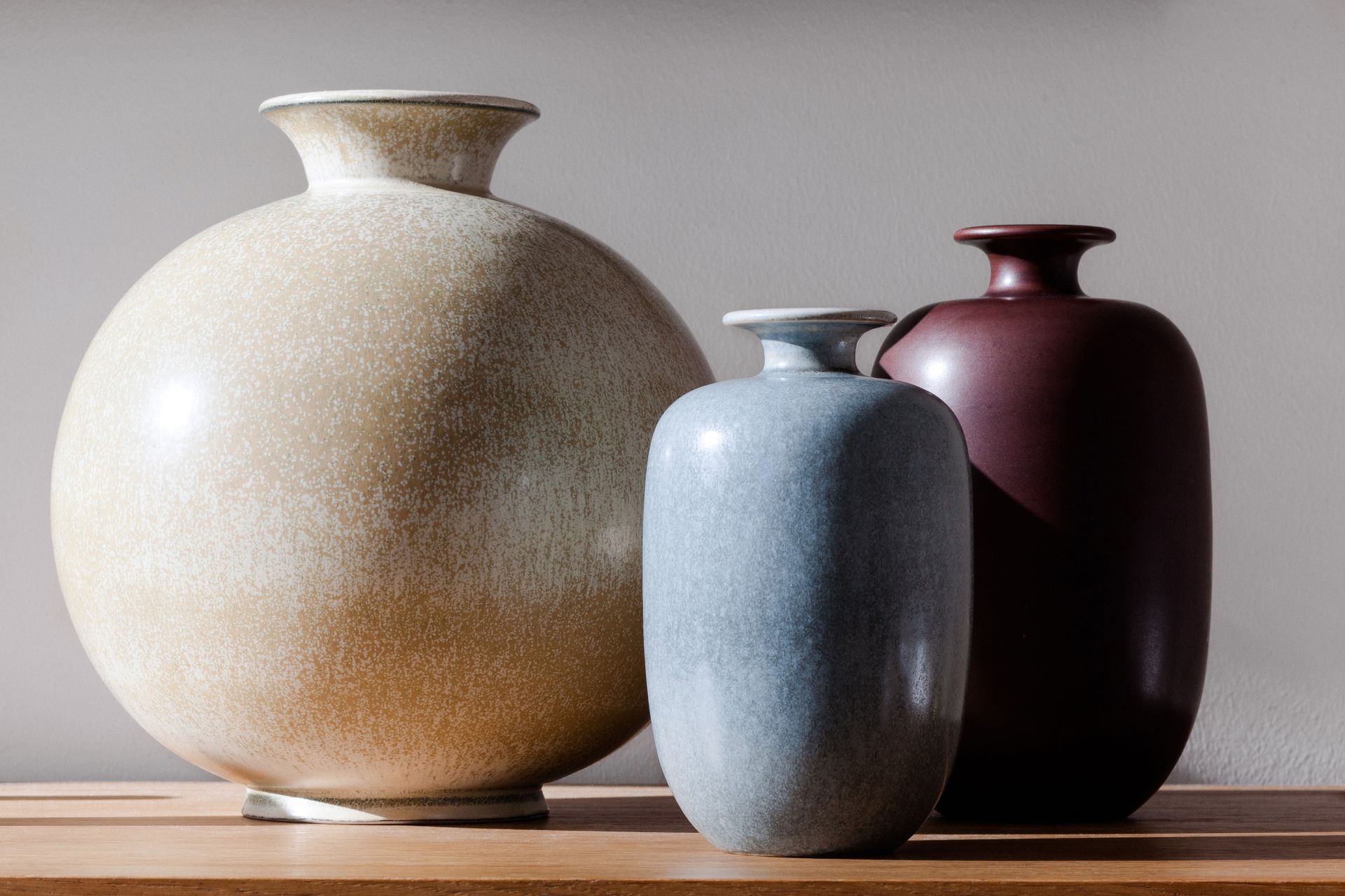 Three vases are sitting on a wooden table.